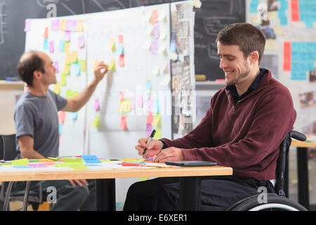 Engineering students posting brainstorming ideas on project board one man with spinal cord injury and other one with Aspergers Stock Photo