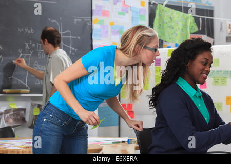Engineering instructor writing math equations on blackboard while students plan project the man with Aspergers Stock Photo