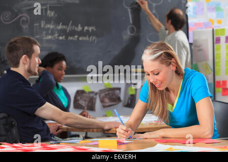 Engineering instructor working on flowchart on blackboard while students working on project one man with spinal cord injury and other one with Aspergers Stock Photo