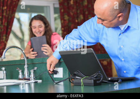 Father plugging in his computer and daughter using tablet Stock Photo