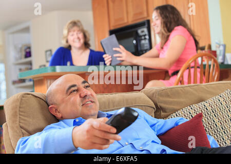 Father using remote with TV and daughter using tablet Stock Photo