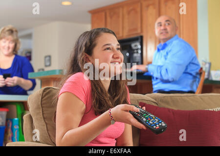 Daughter using TV remote with father using laptop and mother using phone Stock Photo
