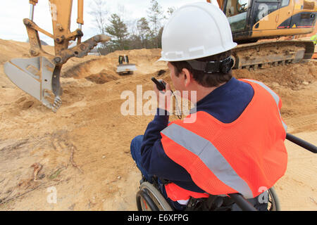 Construction engineer with spinal cord injury talking on portable radio with equipment operators Stock Photo