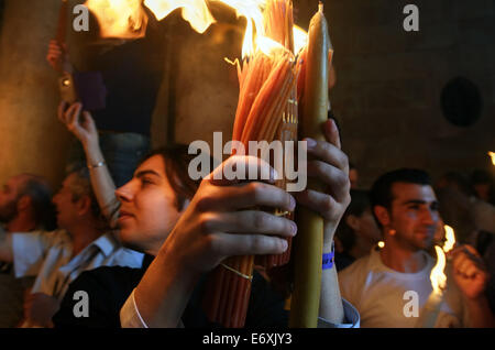 Young priest holds candles with fire in Church of the Holy Sepulchre during Holy Fire ceremony in Jerusalem, Israel Stock Photo