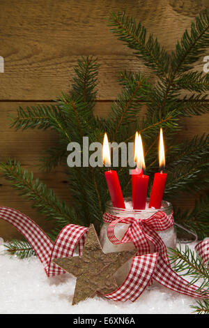 Square Christmas card decorated with four red burning candles, wooden star, snow, ribbon and pine branch Stock Photo