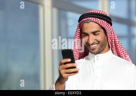 Arab saudi businessman working  with his phone with an office building in the background Stock Photo