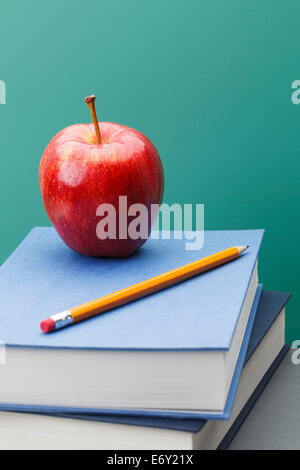 Green Chalkboard, School Books, Sharpened Yellow Pencil and Red Apple in Classroom Setting with Copy Space. Stock Photo
