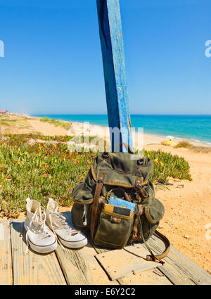 Backpack and shoes on the porch of a wooden hut next to the shore of a European beach. Backpacking traveller taking a break Stock Photo