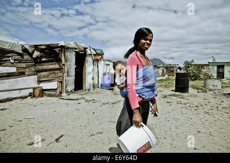Young mother in front of shacks carrying her baby, Langa township, Cape Town, South Africa, Africa Stock Photo