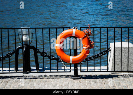 Orange life saving ring on a black pole of the protective fence of the embankment Stock Photo