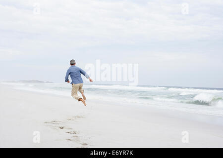 Senior man running and jumping on beach Stock Photo