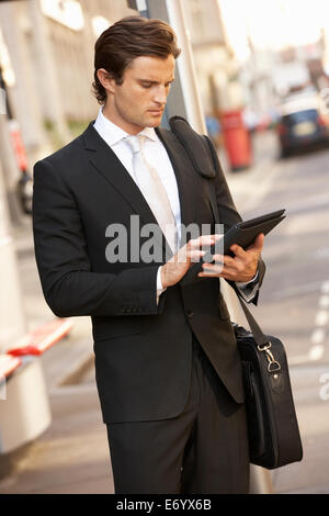 Businessman standing at bus stop using tablet Stock Photo