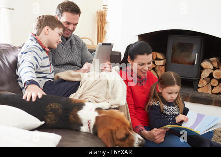 Family Relaxing Reading Book And Using Digital Tablet Stock Photo