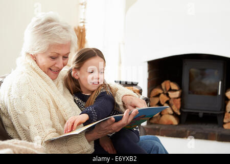 Grandmother And Granddaughter Reading Book At Home Together Stock Photo