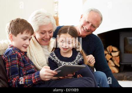 Grandparents Using Digital Tablet On Sofa With Grandchildren Stock Photo