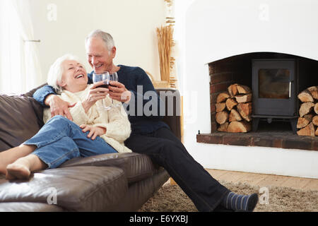 Senior Couple Sitting On Sofa Drinking Red Wine Stock Photo