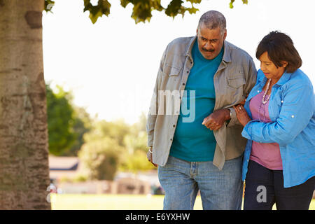 Senior Woman Helping Husband As They Walk In Park Together Stock Photo