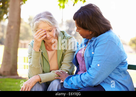 Woman Comforting Unhappy Senior Friend Outdoors Stock Photo