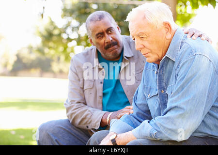 Man Comforting Unhappy Senior Friend Outdoors Stock Photo