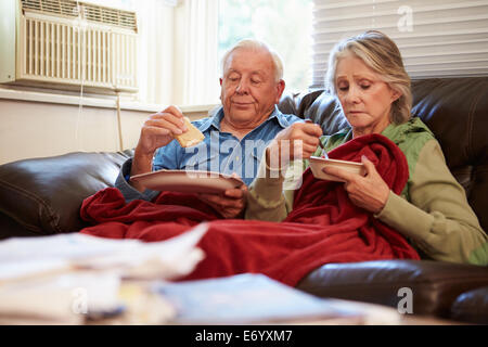 Senior Couple With Poor Diet Keeping Warm Under Blanket Stock Photo