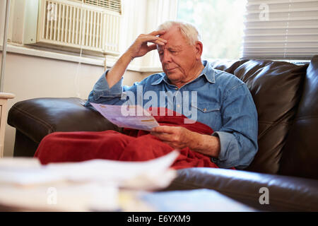 Worried Senior Man Sitting On Sofa Looking At Bills Stock Photo