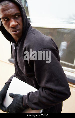 Young Man Breaking Into House And Stealing Laptop Stock Photo