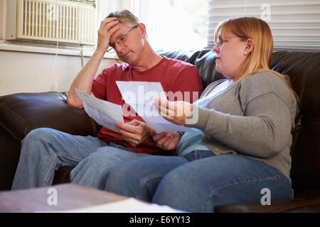 Worried Couple Sitting On Sofa Looking At Bills