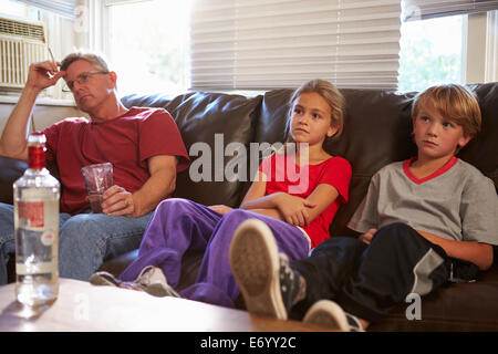 Father Sits On Sofa With Children Smoking And Drinking Stock Photo