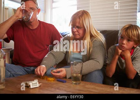 Parents Sit On Sofa With Children Taking Drugs And Drinking Stock Photo