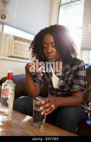 Woman Sitting On Sofa With Bottle Of Vodka And Cigarettes Stock Photo