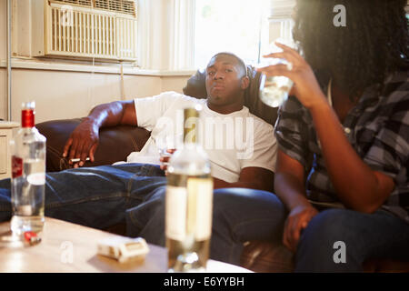 Couple Sitting On Sofa With Bottle Of Vodka And Cigarettes Stock Photo