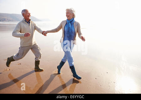 Senior Couple Running Along Winter Beach Stock Photo