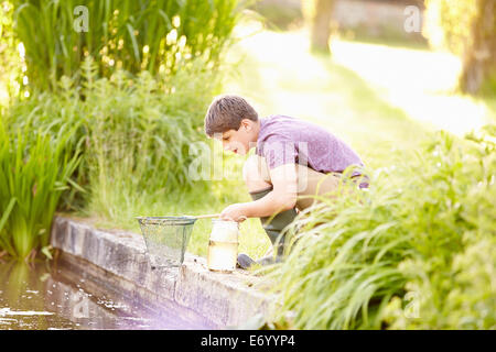 Boy Fishing In Pond With Net And Jar Stock Photo