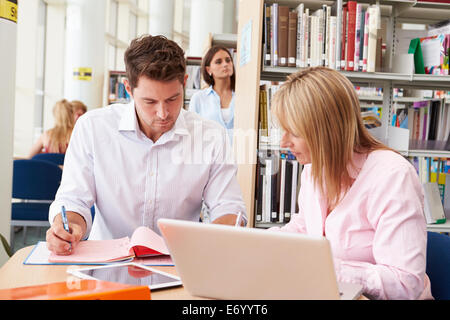 Teacher Helping Mature Student With Studies In Library Stock Photo