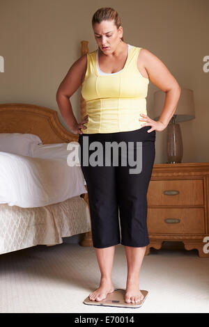 Overweight Woman Weighing Herself On Scales In Bedroom Stock Photo