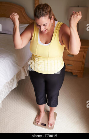 Overweight Woman Weighing Herself On Scales In Bedroom Stock Photo