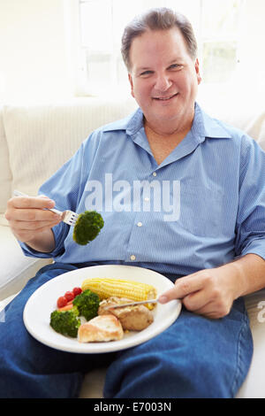 Overweight Man Eating Healthy Meal Sitting On Sofa Stock Photo