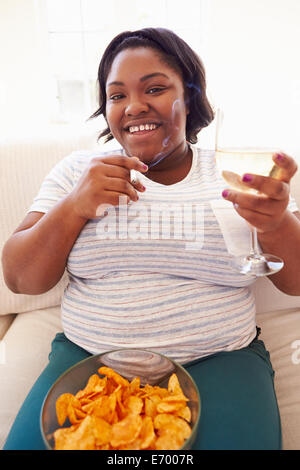 Overweight Woman At Home Eating Chips And Drinking Wine Stock Photo