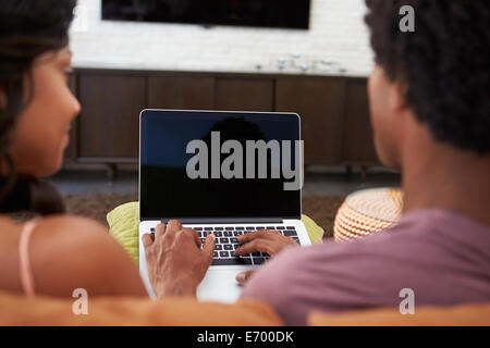 Rear View Of Couple Sitting On Sofa Using Laptop Stock Photo