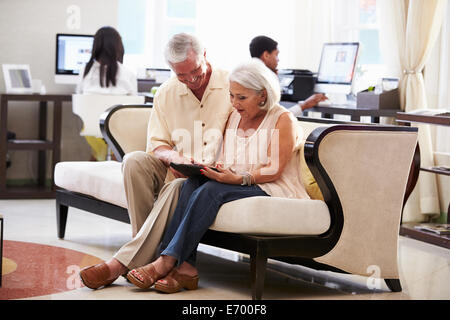 Senior Couple In Hotel Lobby Looking At Digital Tablet Stock Photo