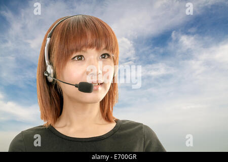 Asian female wearing a headset with microphone, clouds and blue sky in background Stock Photo