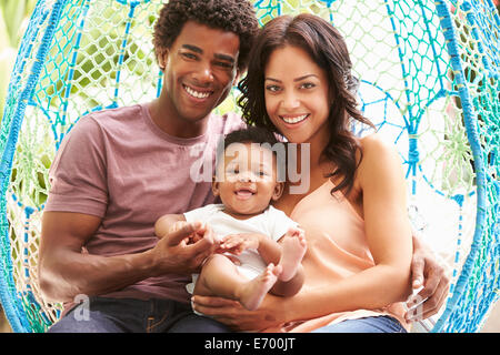 Family With Baby Relaxing On Outdoor Garden Swing Seat