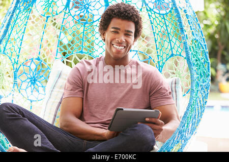 Man On Outdoor Garden Swing Seat Using Digital Tablet Stock Photo
