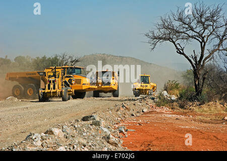 Dump trucks tipping rocks with excavator and grader vehicles working during construction of access road to new platinum mine. South Africa Stock Photo