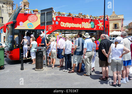 Back view line of tourists boarding & queuing up on a hot summers day to board open top Malta sightseeing tour bus at fishing village of Marsaxlokk Stock Photo