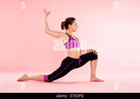Studio shot of young woman in yoga position with legs outstretched and arm raised