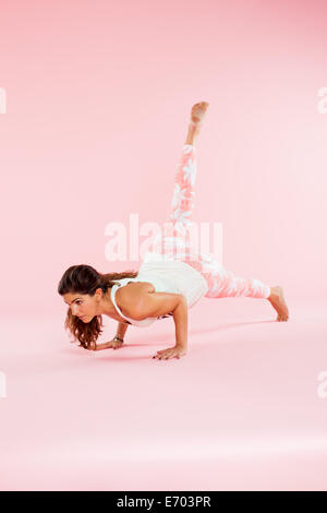 Studio shot of young woman in yoga position balancing with hands on floor and leg raised Stock Photo