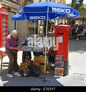 Valletta city centre man setting up a small stall of CDs under parasols beside red UK post box on a hot summers day Republic Street Valletta Malta Stock Photo