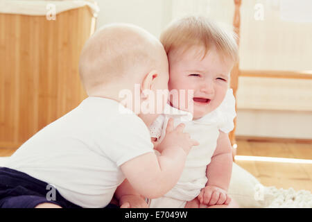 Crying baby girl with baby boy leaning toward her Stock Photo