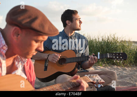 Two adult male friends playing acoustic guitars on Bournemouth beach, Dorset, UK Stock Photo